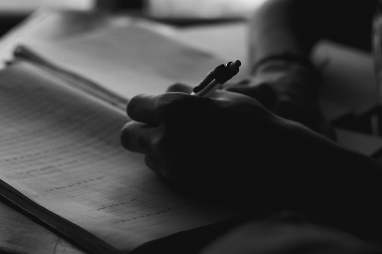 a person holding a pen and writing on a book